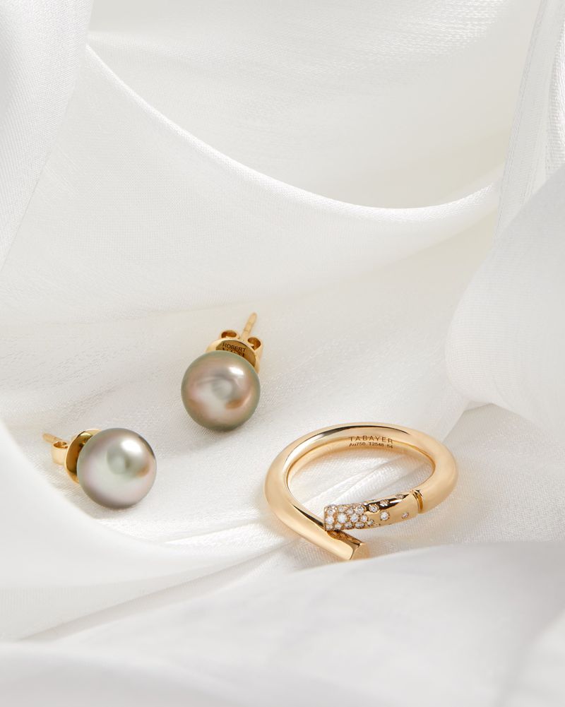 Still-life shot of pearl stud earrings and a gold and diamond ring on a draped white fabric background. Minimalist jewelry.