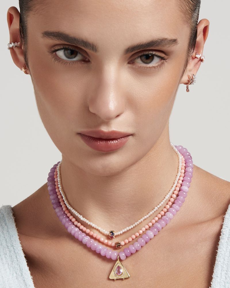 Close-up studio shot of a fair-skinned woman wearing multiple necklaces and ear cuffs against a neutral background.