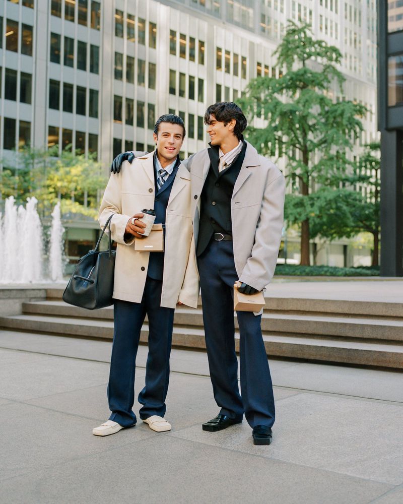 Two men in tailored suits and coats posing outdoors on city steps for Jacquemus