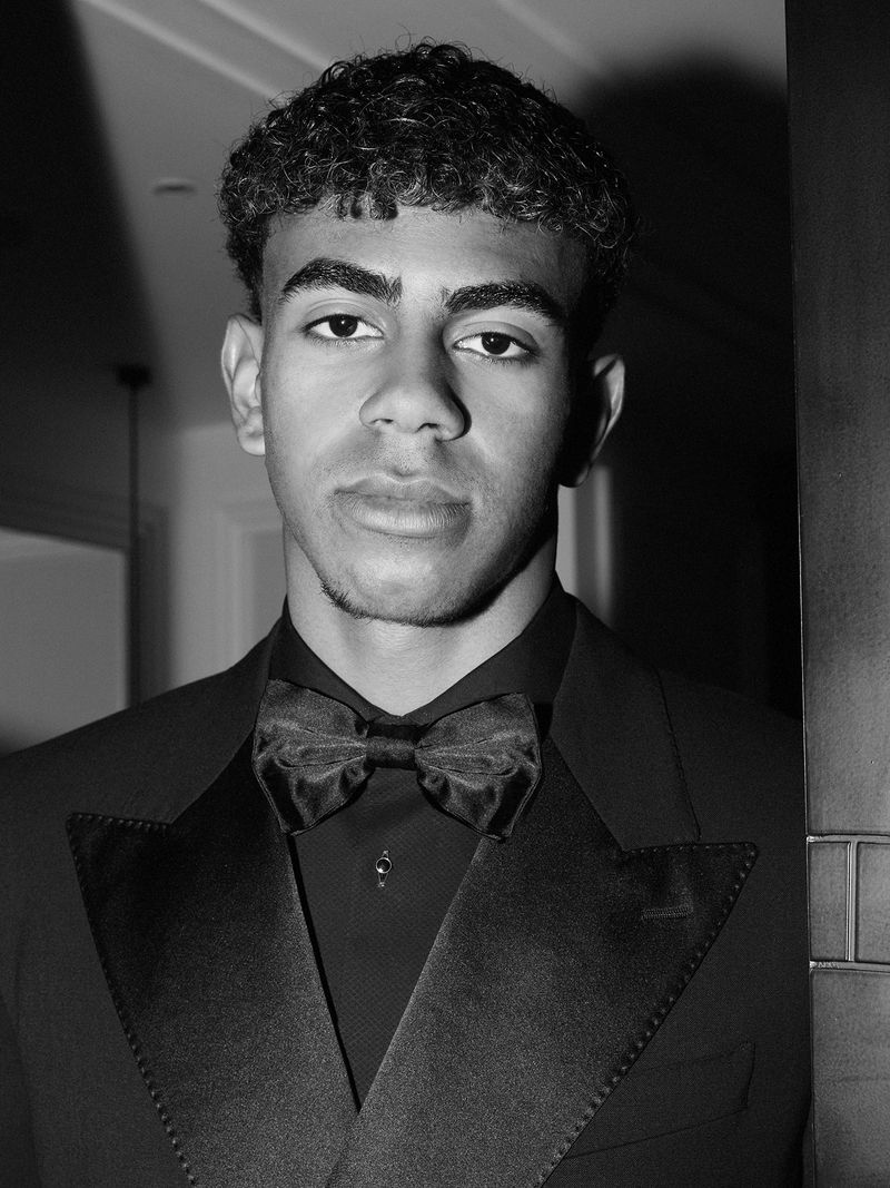 Monochrome portrait of a young adult male wearing a formal bow tie suit, gazing directly at the camera with a serious expression indoors.