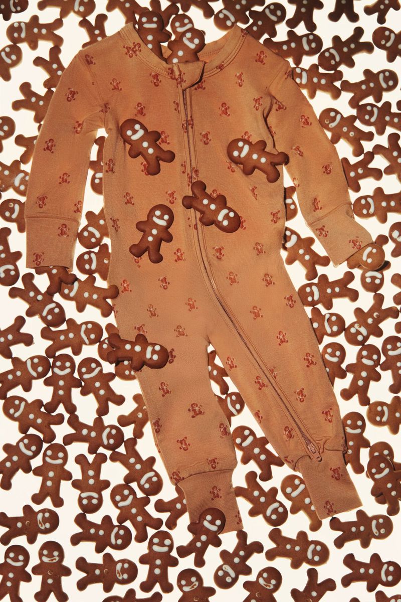 One-piece pajama surrounded by gingerbread man cookies on a white surface, overhead shot, holiday season clothing, cozy sleepwear.