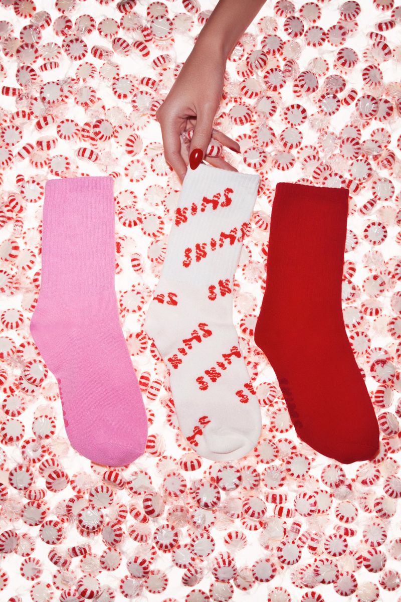Close-up of pink, white, and red socks held by a hand over a background of peppermint candies, showcasing a fashion product in a studio setting.