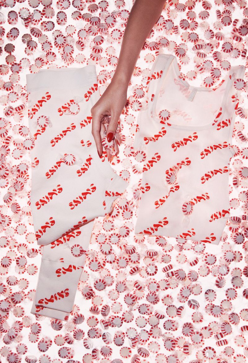 Clothing with a peppermint candy print lies on a surface covered in peppermint candies, with a hand reaching into the shot.