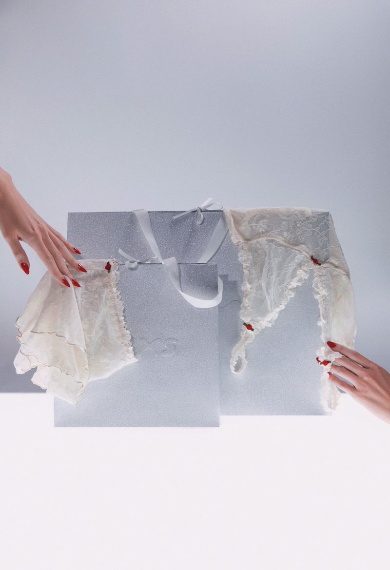 Lingerie displayed on geometric pedestals with hands in frame, set against a bright backdrop showcasing fashion and delicate fabrics.