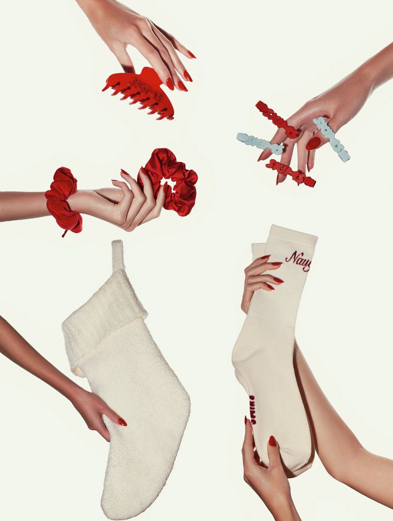 Hands hold Christmas stockings and red hair accessories against a white background in a commercial studio photography setup.