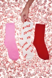Hand holding a white sock with red branding over pink, white, and red socks arranged on a bed of peppermint candies.