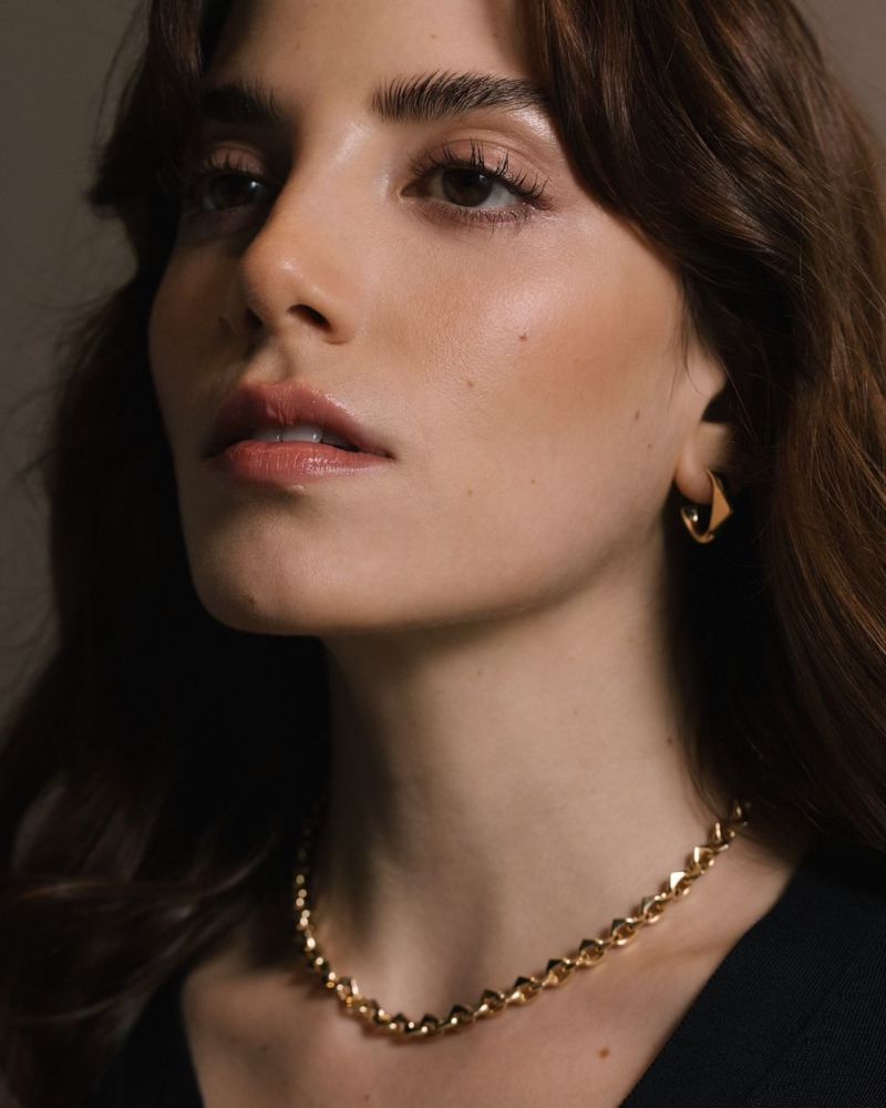 Close-up portrait of a woman wearing gold hoop earrings and a gold chain necklace for the Prada Eternal Gold collection.
