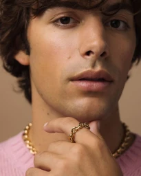 Close-up portrait of a man wearing a gold chain necklace and ring against a neutral background for Prada Eternal Gold