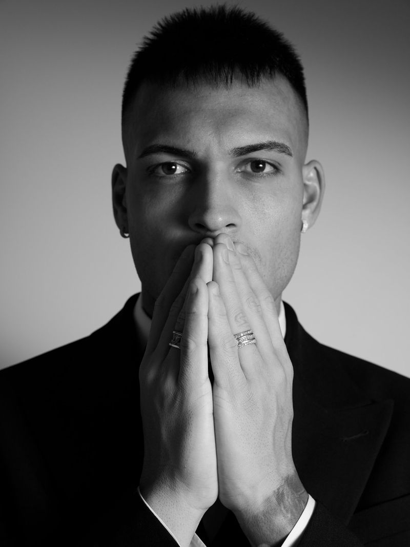 Black and white portrait of an adult male in a dark suit with hands raised to his face in an indoor photo studio.