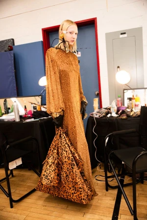 Model in a leopard print dress holding a matching oversized bag in a backstage dressing room