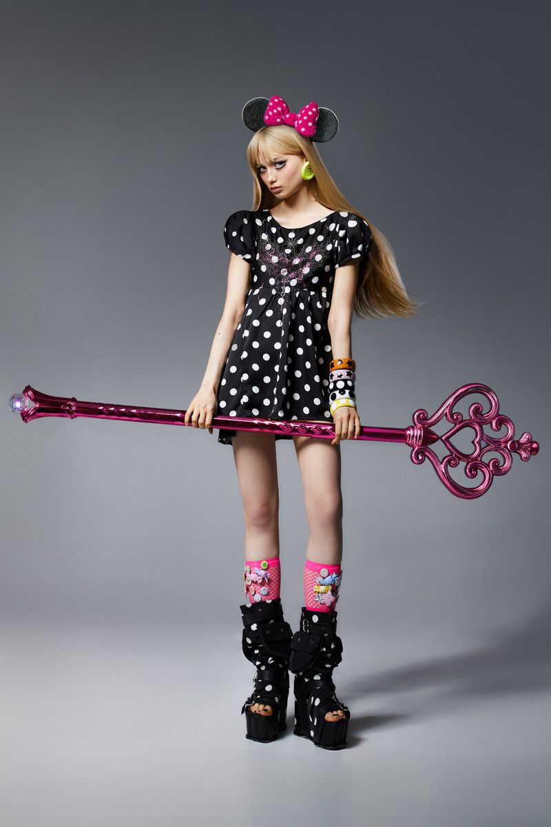 Young woman in polka-dot dress and platform boots holds a decorative key in a studio shot, against a gray backdrop.
