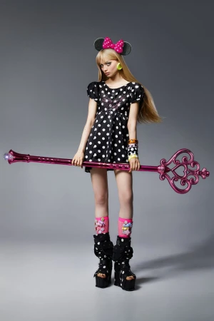 Young woman in polka-dot dress and platform boots holds a decorative key in a studio shot, against a gray backdrop.