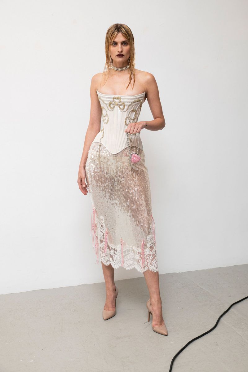 Elegant fashion photo features a blonde woman in a corset and beaded dress posing in a studio with wet hair and nude high heels.