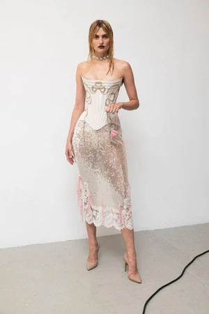 Model in a structured white corset top and shimmering sequin skirt posing against a plain white studio backdrop.