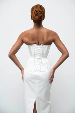 Rear view of a model wearing a structured white corset and matching skirt against a plain background.