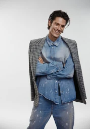 Smiling male model wearing a denim shirt and jacket draped over shoulders against a white background for Simons Canada.