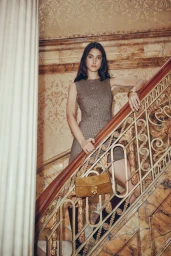 Model standing on an ornate staircase wearing a brown tweed dress and holding a suede handbag for Simons Canada.