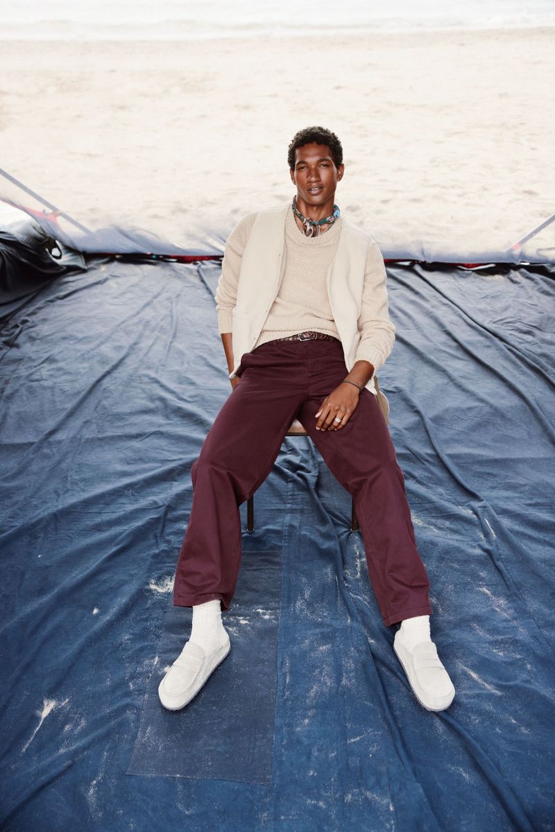 A well-lit, full shot of a man sitting on a chair, wearing a cardigan and trousers on a blue tarp, shot in daylight.