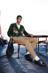 Model Joshua Seth seated in a green floral embroidered cardigan, tan trousers, and black loafers for Simons Canada menswear.
