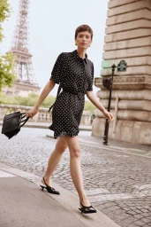 Model Loane Normand walks along a Paris cobblestone street in a black polka dot dress and slingback heels with the Eiffel Tower behind.