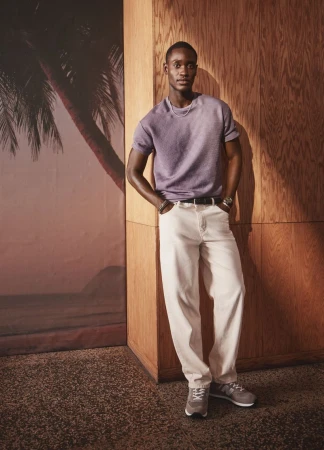 Model Charles Oduro wearing lavender t-shirt and white jeans against wood paneling and palm mural for Simons Canada