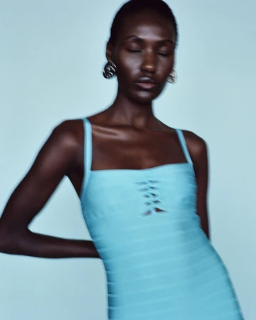 Elegant portrait of a Black woman with closed eyes, wearing a form-fitting aqua dress and statement earrings against a light blue background.