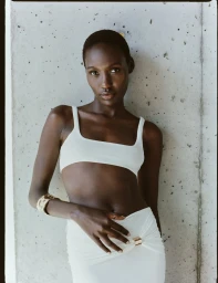 Model wearing white top and skirt standing against a textured concrete wall for Herve Leger Spring Summer 25
