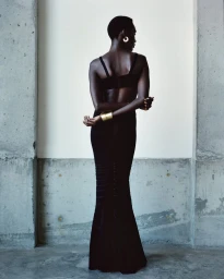 Model wearing a black evening dress standing against concrete pillars with a light background for Herve Leger spring summer 25.