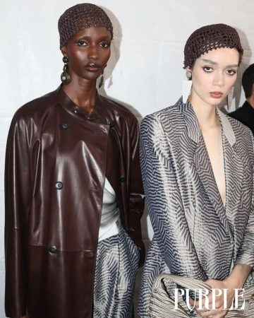 Two fashion models pose in patterned blazers with matching headwear. The model on the left wears a brown leather jacket.