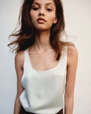 Model wearing a light-coloured scoop-neck top against a plain white background in a studio setting.
