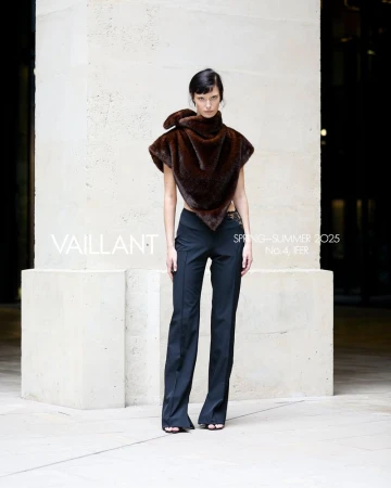 Model standing in architectural stone setting wearing a dark brown asymmetrical top and black trousers for Vaillant Spring-Summer 2025.