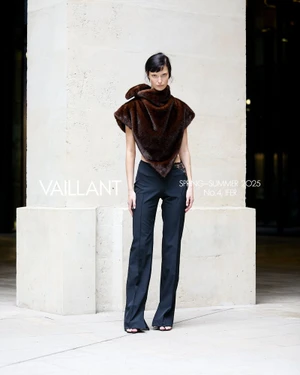 Model standing in architectural stone setting wearing a dark brown asymmetrical top and black trousers for Vaillant Spring-Summer 2025.