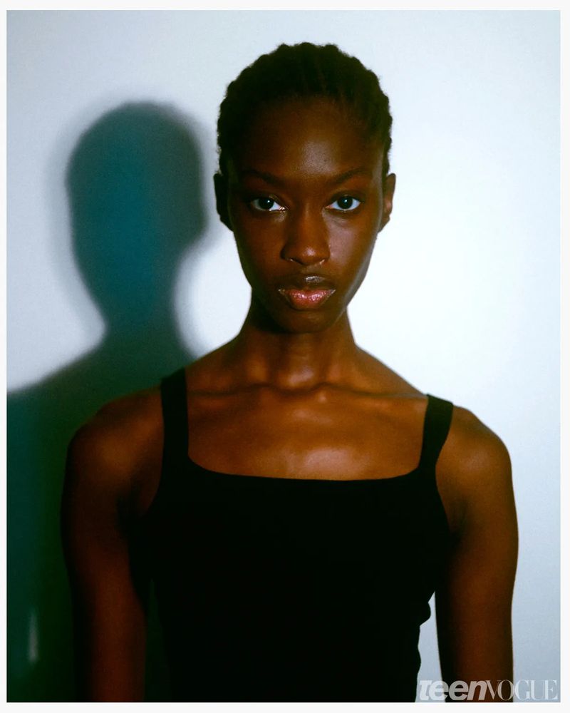 Close-up portrait of a young Black woman with shoulder-length braided hair, wearing a black tank top against a white background.