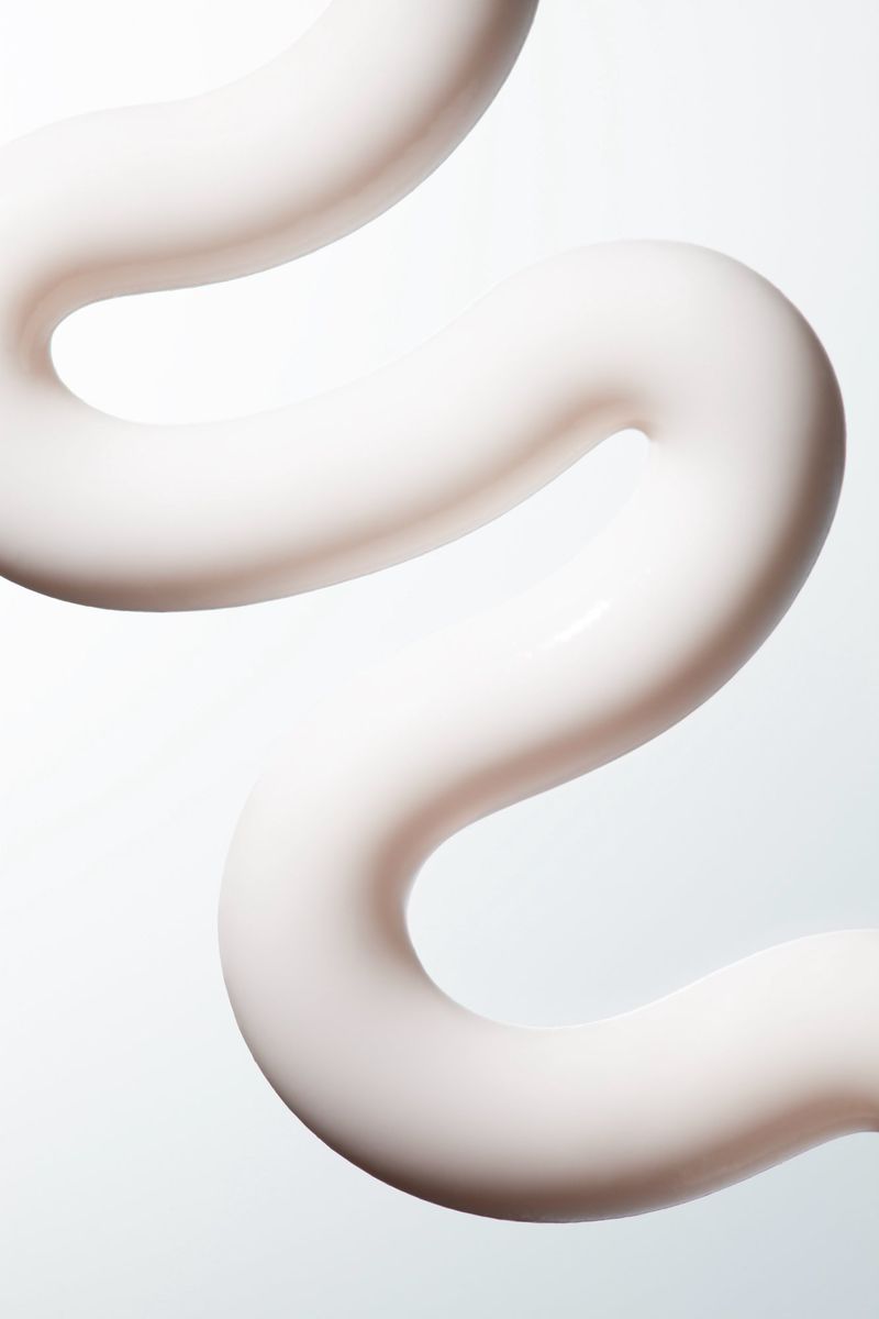 Close-up of a wavy, creamy-white textured skincare product on a pale gradient backdrop in a studio setting. Beauty shot for advertising.