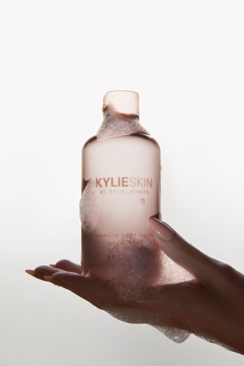Kylie Skin vanilla body wash in clear bottle with bubbles, held in a hand against a bright white background.