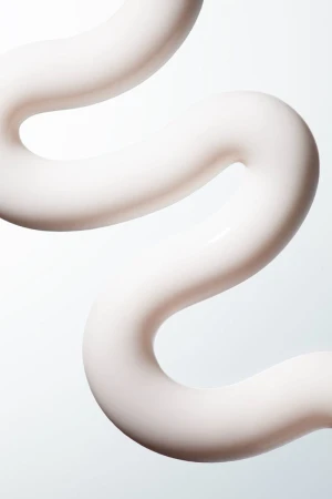 Close-up macro shot of smooth white cream product swatch curving against a clean white seamless background.