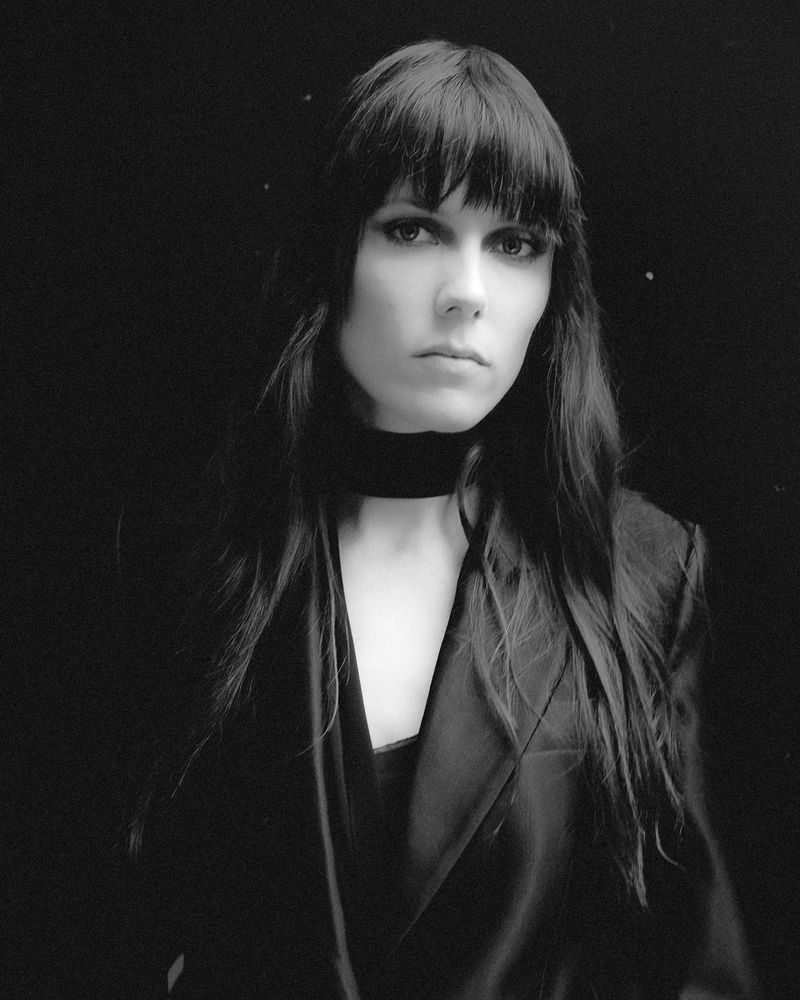 Portrait of a model with dark long hair wearing a black jacket and choker against a dark background