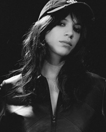 Portrait of a model wearing a cap and dark zip jacket in a black and white editorial shoot by Daniele Fummo for Aaron Esh.