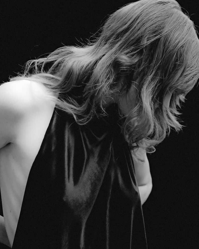 Black and white portrait of a female with long hair draped with a dark fabric against a dark background.