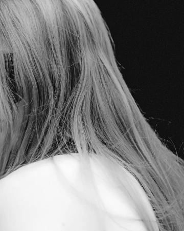 Close-up of a model's long blonde hair flowing over a bare shoulder against a solid black background.