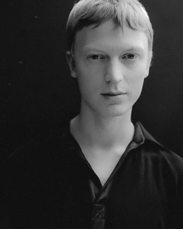 Monochrome portrait of a young man wearing a dark collared shirt against a dark backdrop for Aaron Esh