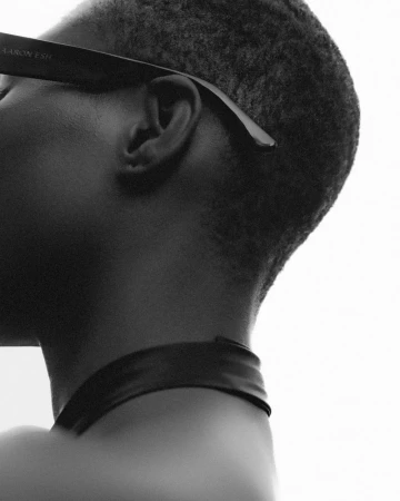 Close-up monochrome profile portrait of a model wearing dark sunglasses against a bright background