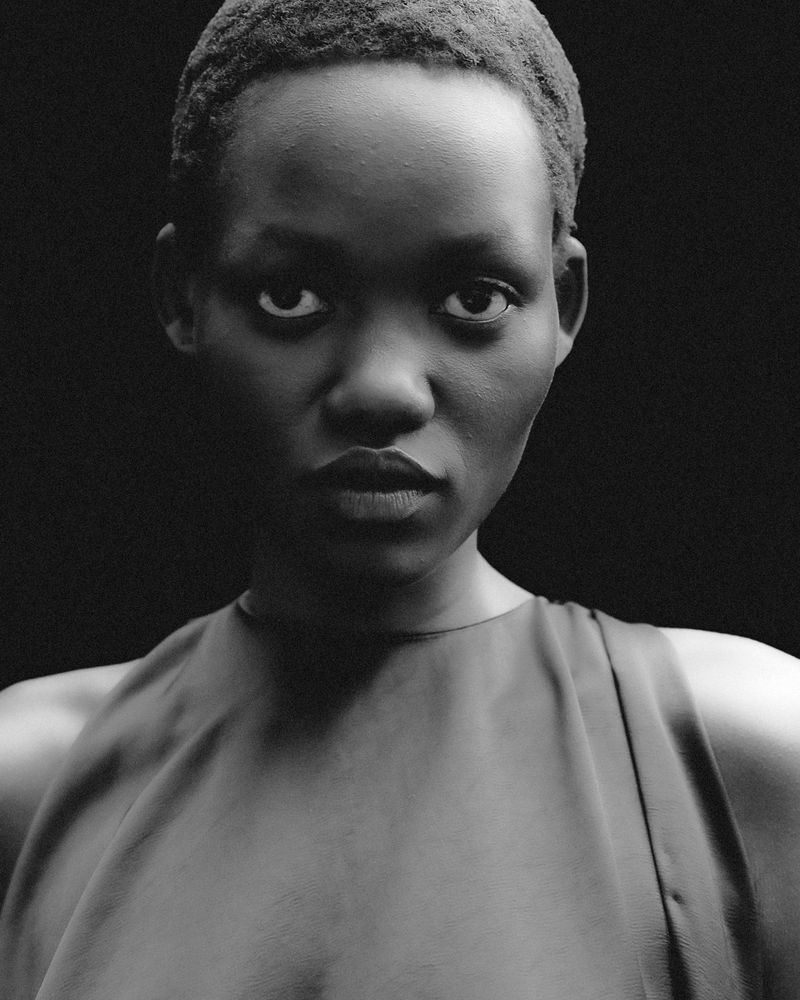 Close-up monochrome portrait of a model with short textured hair wearing a sleeveless top against a dark background