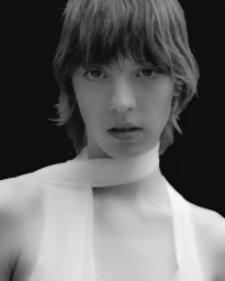 Portrait of a model wearing a white top and neck scarf against a black background shot by Daniele Fummo for Aaron Esh S/S 25
