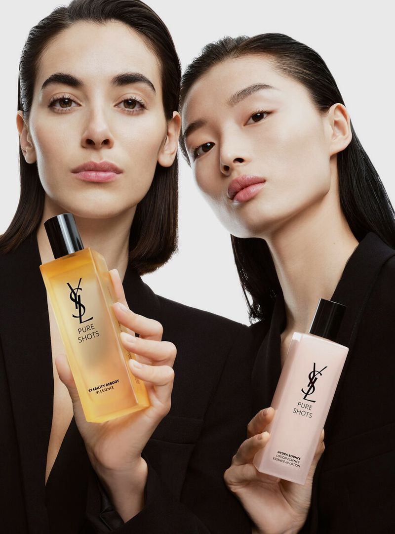 Two women pose indoors with YSL Pure Shots skincare products in a beauty shot, emphasizing natural light and skin tones against a clean backdrop.
