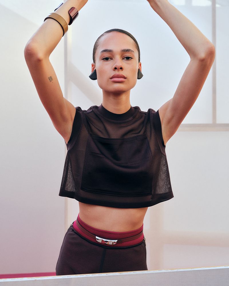 Athletic woman in workout gear poses in a bright studio with her arms raised, showcasing fitness and fashion-forward activewear.