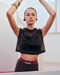 Model posing with arms raised, wearing a black mesh top and layered cuffs for Hermès Spring/Summer 2025.