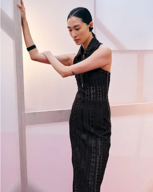 Model in a black patterned dress leaning against a translucent framework structure at the Hermes spring summer 25 show