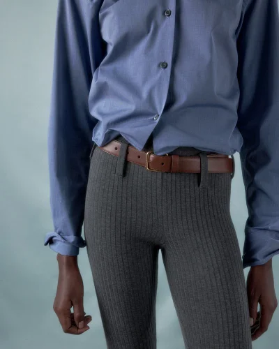 Model wearing a blue button-down shirt and grey ribbed trousers with a brown leather belt against a neutral background