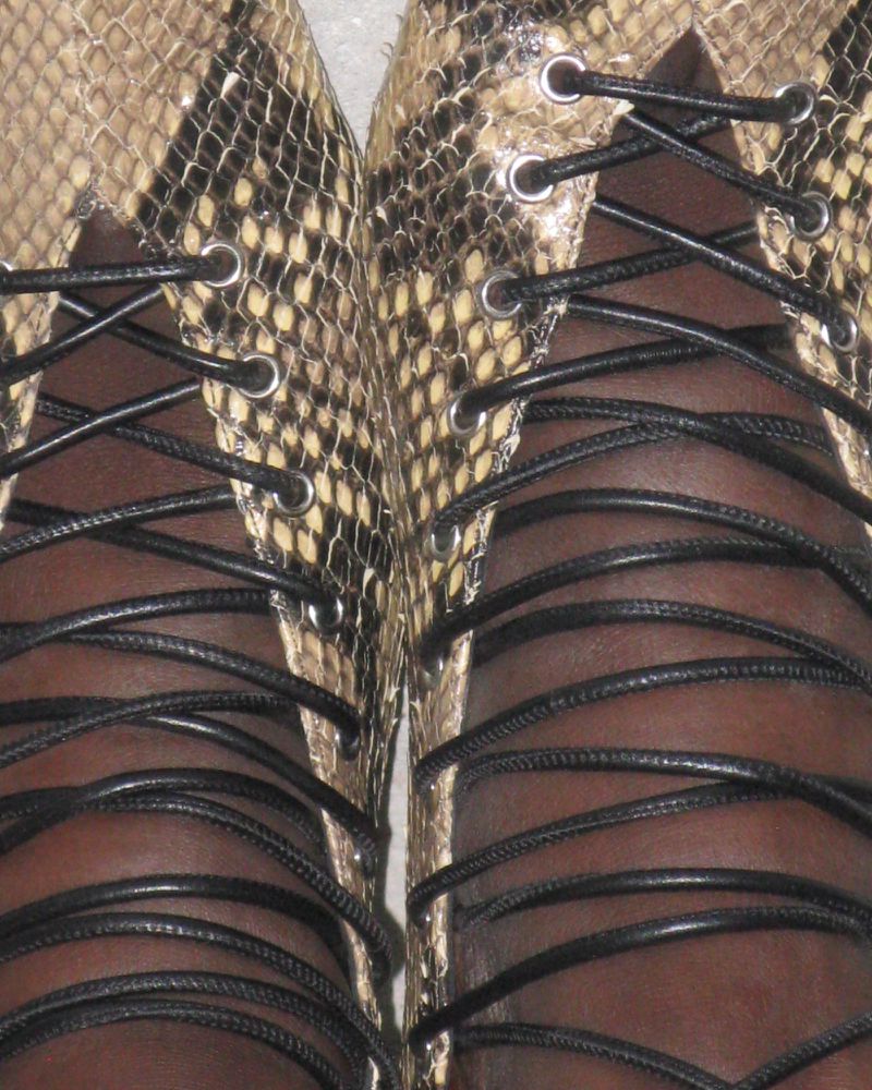 Close-up of two feet in tan and black snakeskin lace-up shoes with black laces. Focus on the shoes and shoelaces, indoors.